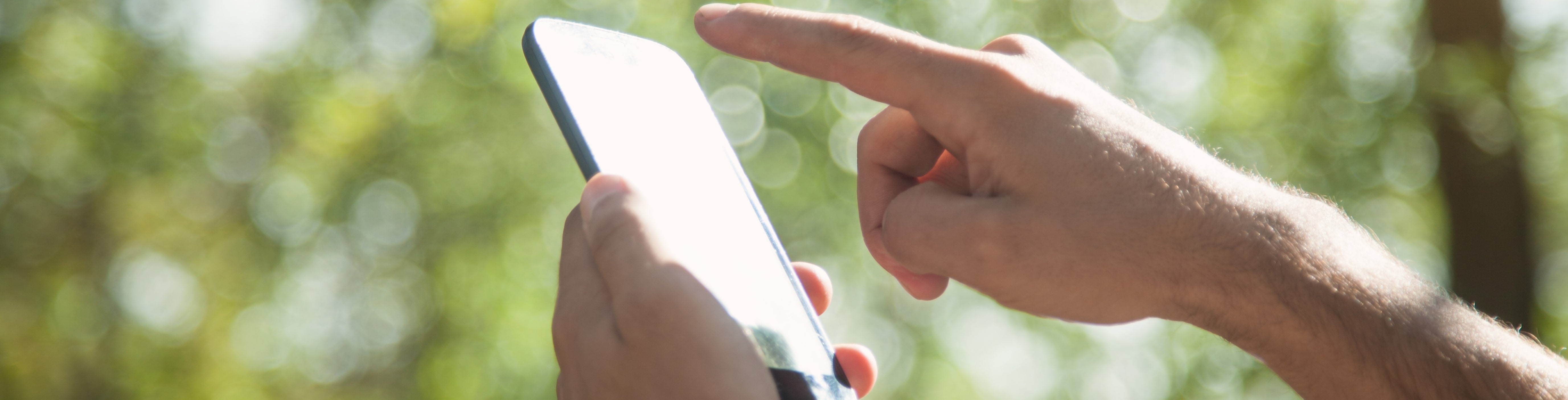 smartphone with index finger and blurred nature background